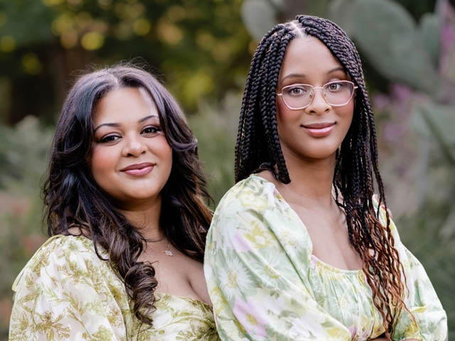 An African American woman and her daughter, both in floral print dresses, pose side by side for the camera.