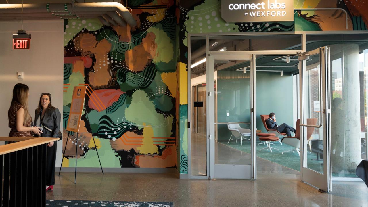 People mingle outside the entrance to office space that has a sign above it that reads "Connect Labs by Wexford".