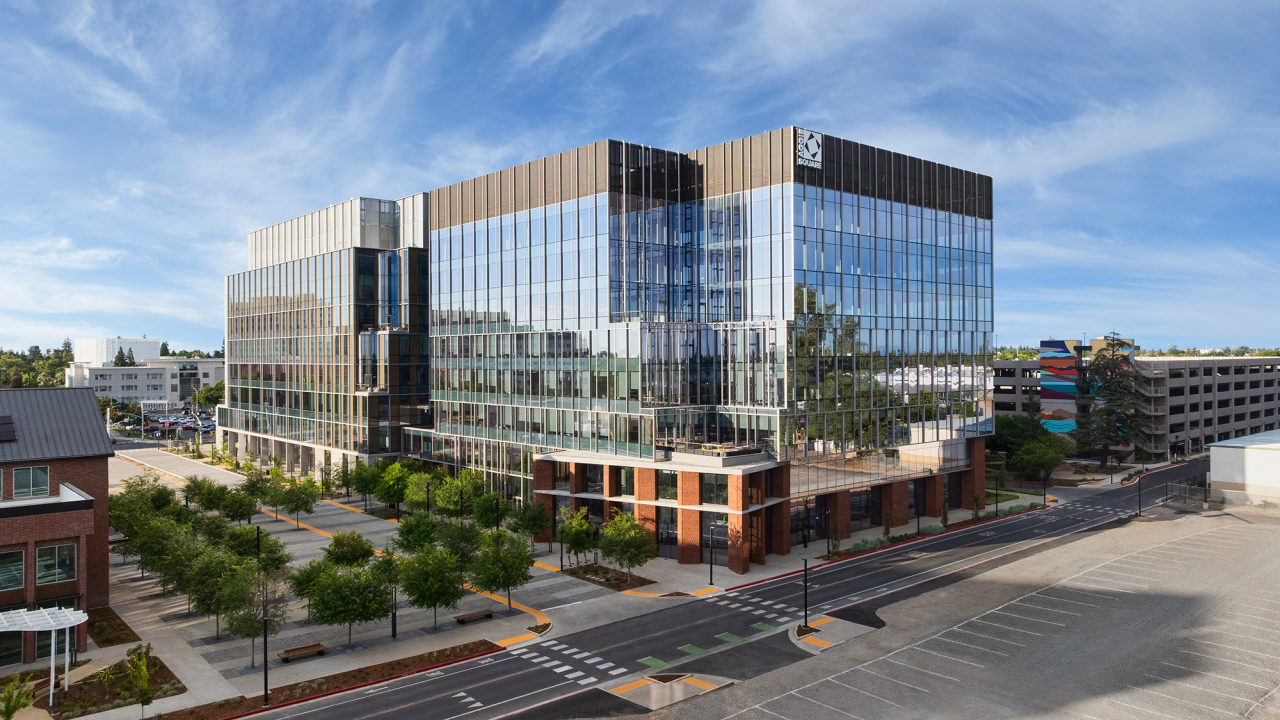 Modern mirrored-glass office complex with plaza, trees and street under blue sky