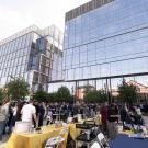 Hundreds of people mingling outside a glass and brick building with tables set up showcasing different organizations.