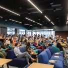 A large group of individuals seated in an auditorium listening to a presenter.