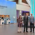 Three adults stand in a spacious exhibition hall with a tall blue-lit column and booths.